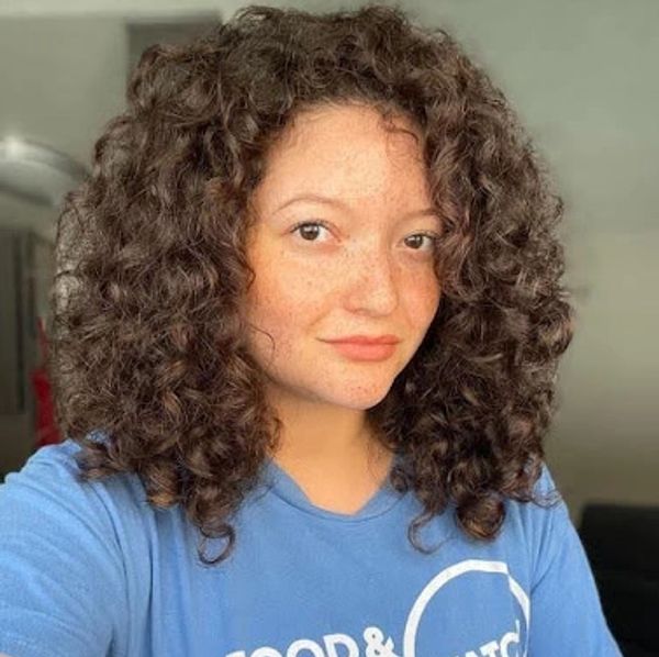 Young woman with curly hair wearing a blue t-shirt.