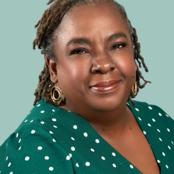 Portrait of a smiling woman with dreadlocks wearing a green polka-dot top.
