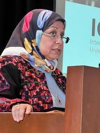 Woman speaking at a podium wearing a colorful headscarf.