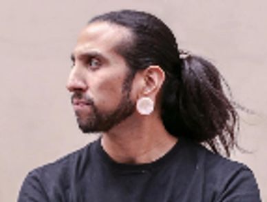 Man with long hair tied back and large ear gauges.