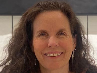 Smiling woman with long brown hair and silver earrings.