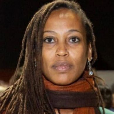 Portrait of a woman with long dreadlocks and a serious expression.