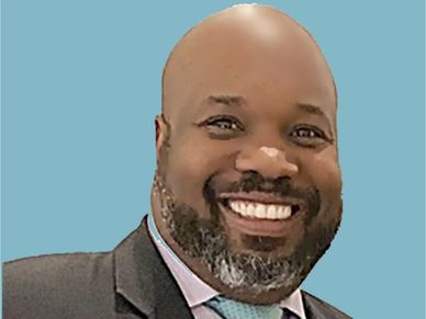 Smiling man with a beard in a suit against a blue background.