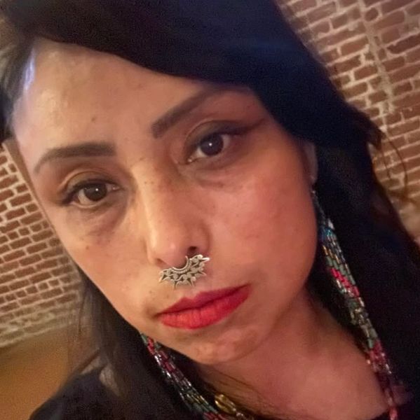 Close-up of a woman with a decorative septum ring and colorful beaded earrings.