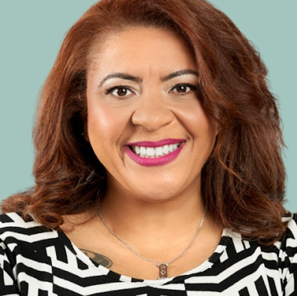 Smiling woman with curly auburn hair and bright lipstick against a blue background.