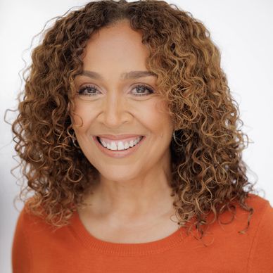Smiling woman with curly hair and orange top.