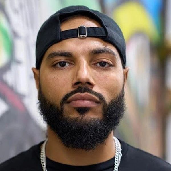 Bearded man wearing a black cap and chain necklace.