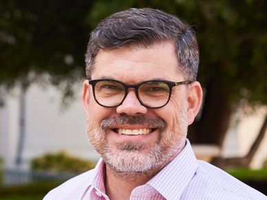 Smiling man with glasses and beard outdoors.