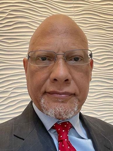 Man with glasses and a red tie against a textured wall.