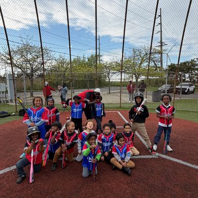 Youth baseball team posing with bats on a field behind a net.