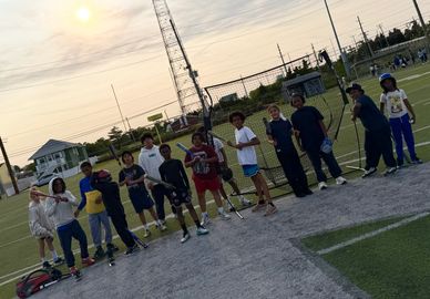 A group of boys posing with baseball bats on a field at sunset.