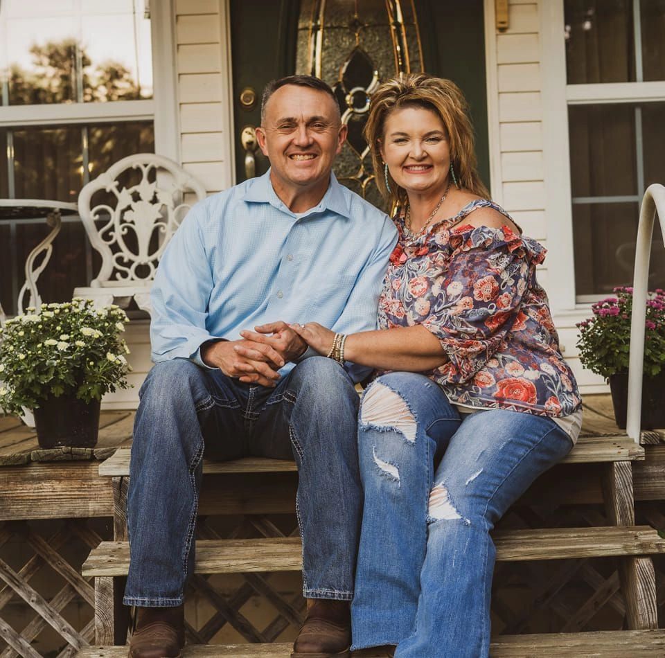Smiling couple sitting on wooden steps outside a house with flowers.