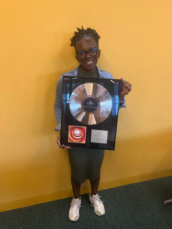 Person smiling and holding a music award plaque against a yellow wall.