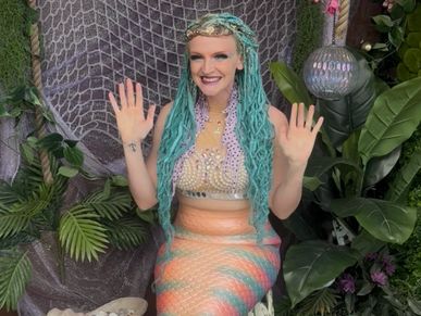 A woman dressed as a colorful mermaid with blue hair and a beaded top.