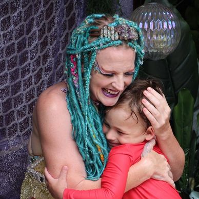 Woman with turquoise dreadlocks hugging a smiling child in red.