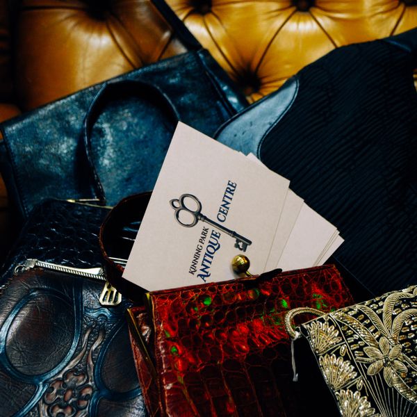 Vintage handbags and business cards from Kunning Park Antique Centre on a leather surface.