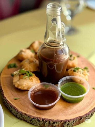 Indian snack pani puri with tamarind and mint chutney served on wooden platter.