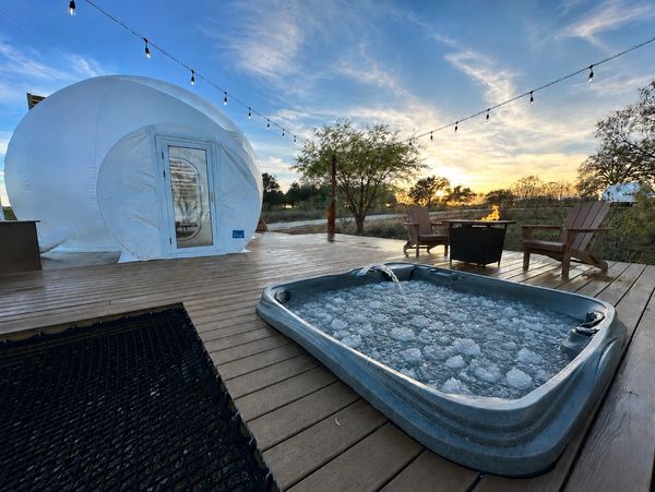 Outdoor deck with bubble tent and hot tub at sunset.