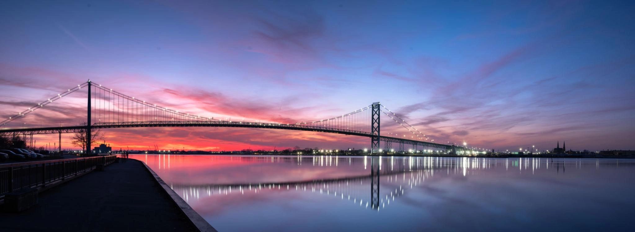 Suspension bridge at sunset with colorful sky reflection.