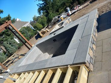 A modern outdoor fire pit under construction in a backyard.