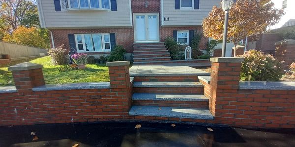 Front of a brick house with steps and a garden in autumn.