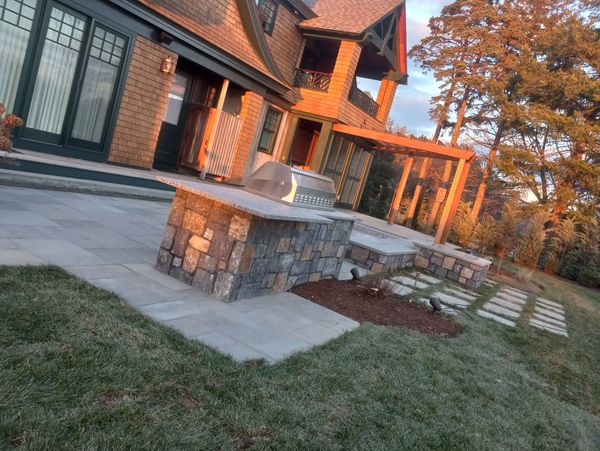 Outdoor patio with stone grill and wooden pergola at sunset.
