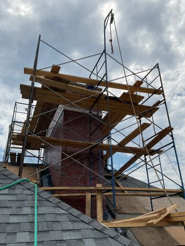 Scaffolding around a brick chimney on a roof under cloudy sky.