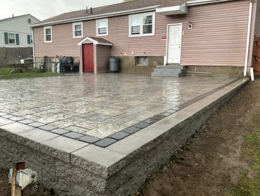 Newly constructed raised patio with stone tiles behind a house on a rainy day.