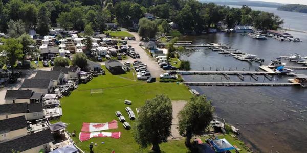 A lakeside campground with RVs, docks, and a large Canadian flag on the grass.