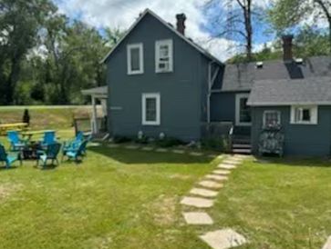 A blue two-story house with a stone path leading to a lawn seating area.