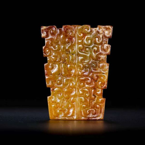 Carved jade artifact with intricate swirling patterns on a tapered rectangular shape.