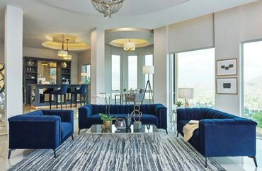 Modern living room with blue velvet sofas and large windows.