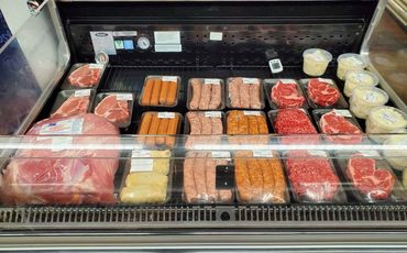 Display case filled with various cuts of raw meat and packaged sausages.