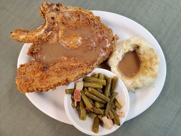 Fried pork chop with mashed potatoes, gravy, and green beans.