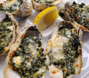 Baked oysters topped with spinach and cheese, served with a lemon wedge.