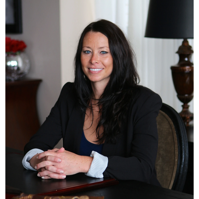Professional woman with dark hair smiling at the camera, seated at a desk.