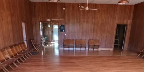 A spacious wooden room with chairs lined along the walls and wooden flooring.