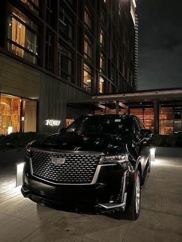 Black Cadillac SUV parked at night outside a modern building.