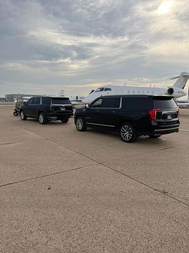 Two black SUVs parked near a private jet on an airport tarmac at sunset.