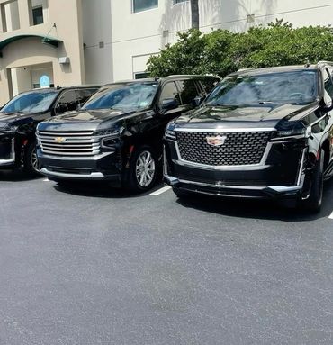 Three black luxury SUVs parked side by side in a sunny lot.