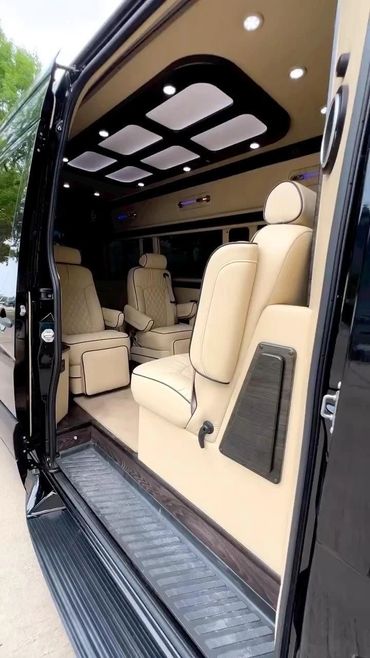 Luxurious beige leather seats inside a black van with ambient ceiling lights.