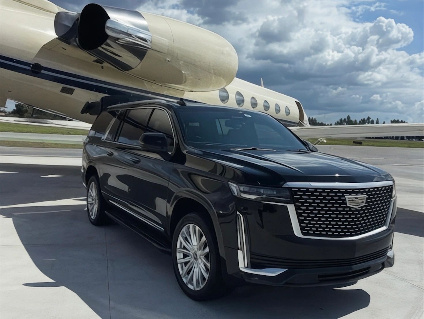 Black luxury SUV parked near a private jet under a cloudy sky.
