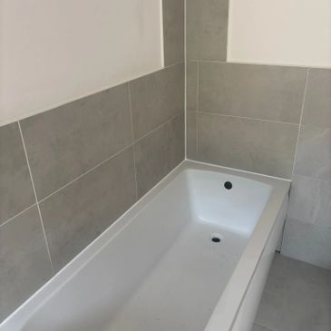 A clean white bathtub with gray tiled walls in a bathroom corner.