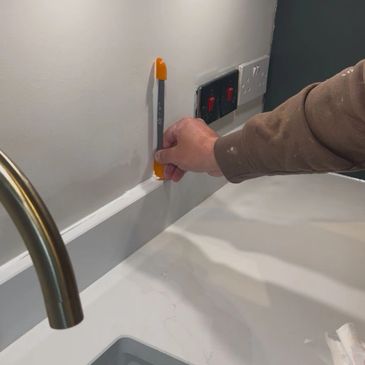 Person using a tool to mark a wall above a kitchen counter.