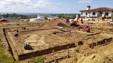 Excavation work for a new building foundation near residential homes with ocean view.