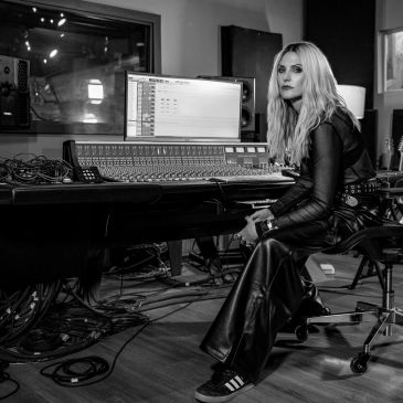 Woman seated in a music studio, surrounded by audio equipment.
