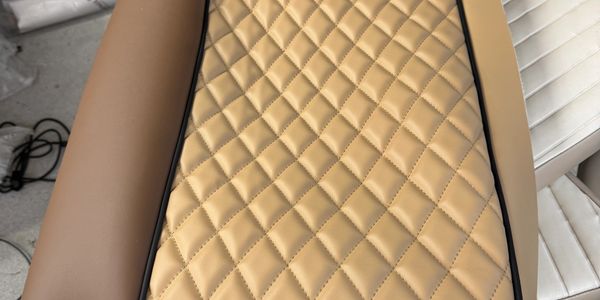 Close-up of tan quilted leather upholstery with black piping detail.
