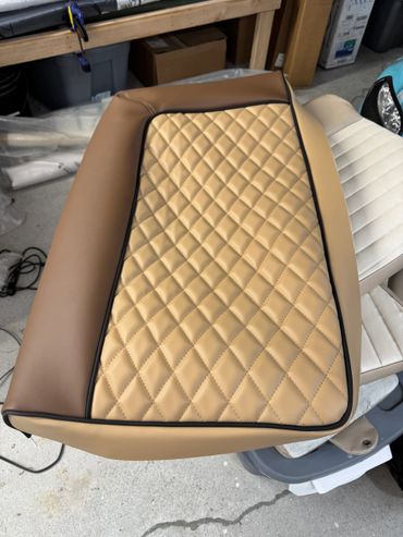 Close-up of tan quilted leather upholstery with black piping detail.