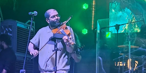 Man playing violin on stage under green lights.