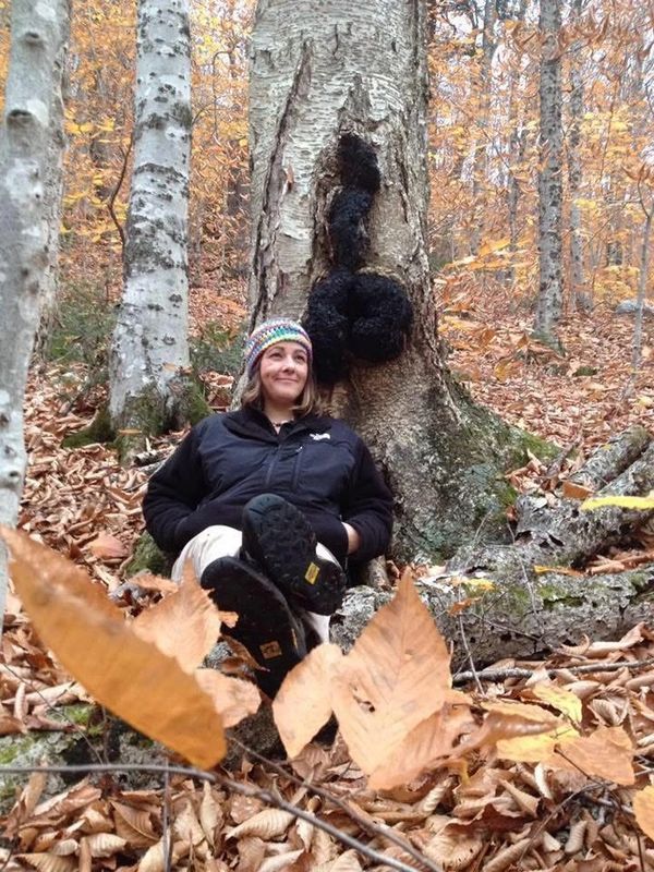 Woman sitting against a tree with black fungus in a forest.